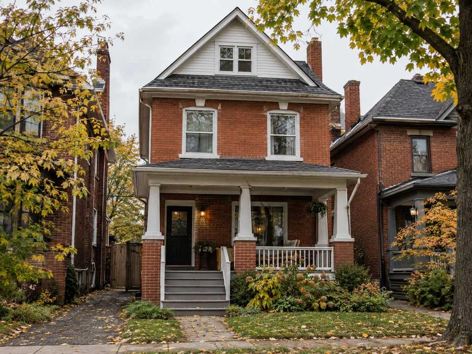 A red-brick house from about 1910 with a deep front porch on a tree-lined lower-city Hamilton street